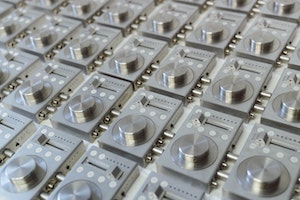 An large number of metallic devices, layed out in an orderly pattern. Each has a large knob at the bottom, 4 buttons and a horizontal slider at the top.